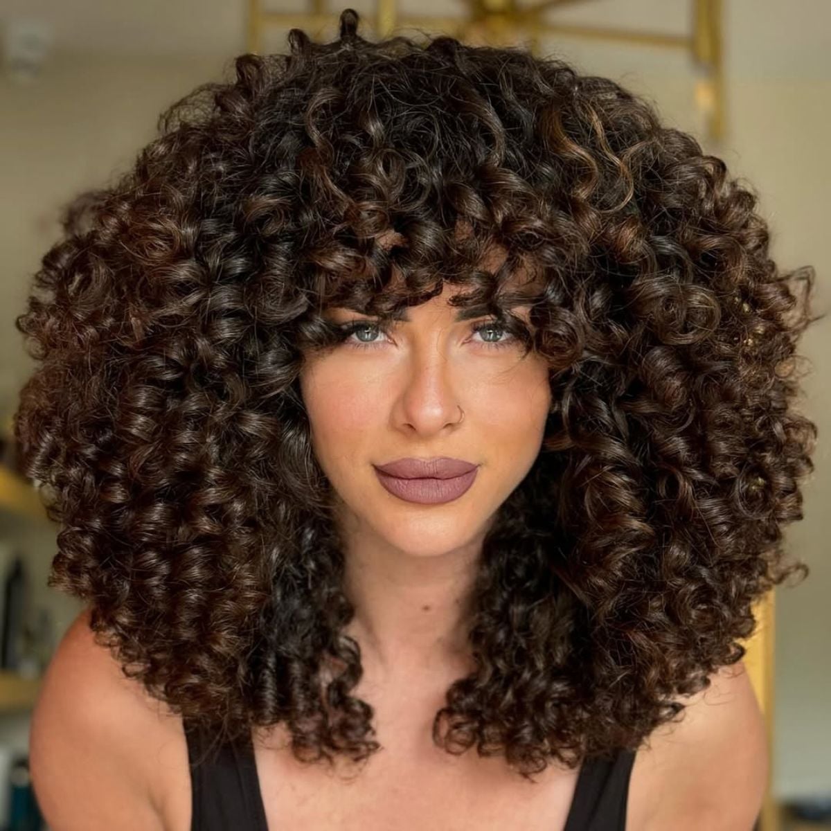 Voluminous Dark Brown Curls With Blonde Highlights and Curtain Bangs — Trendy Shoulder Length Curly Hair